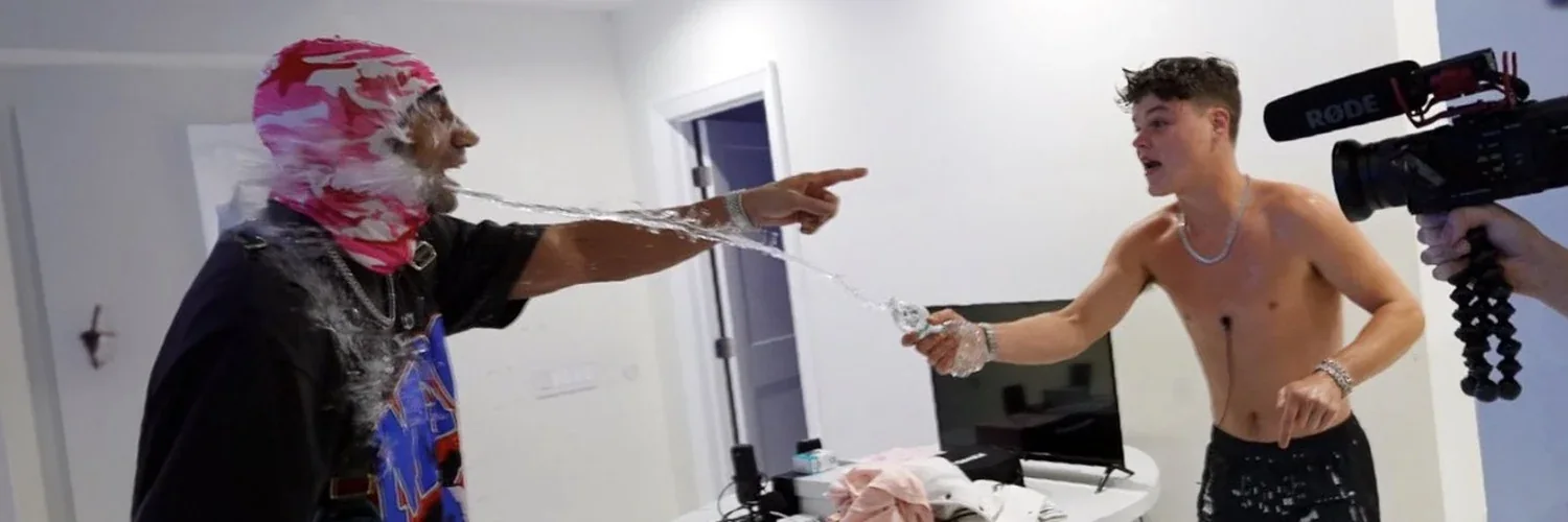 Two people in a room, water flying from a bottle and a camera in the foreground.